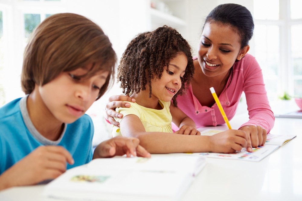 Two children and an adult sit together at a table, working on schoolwork.