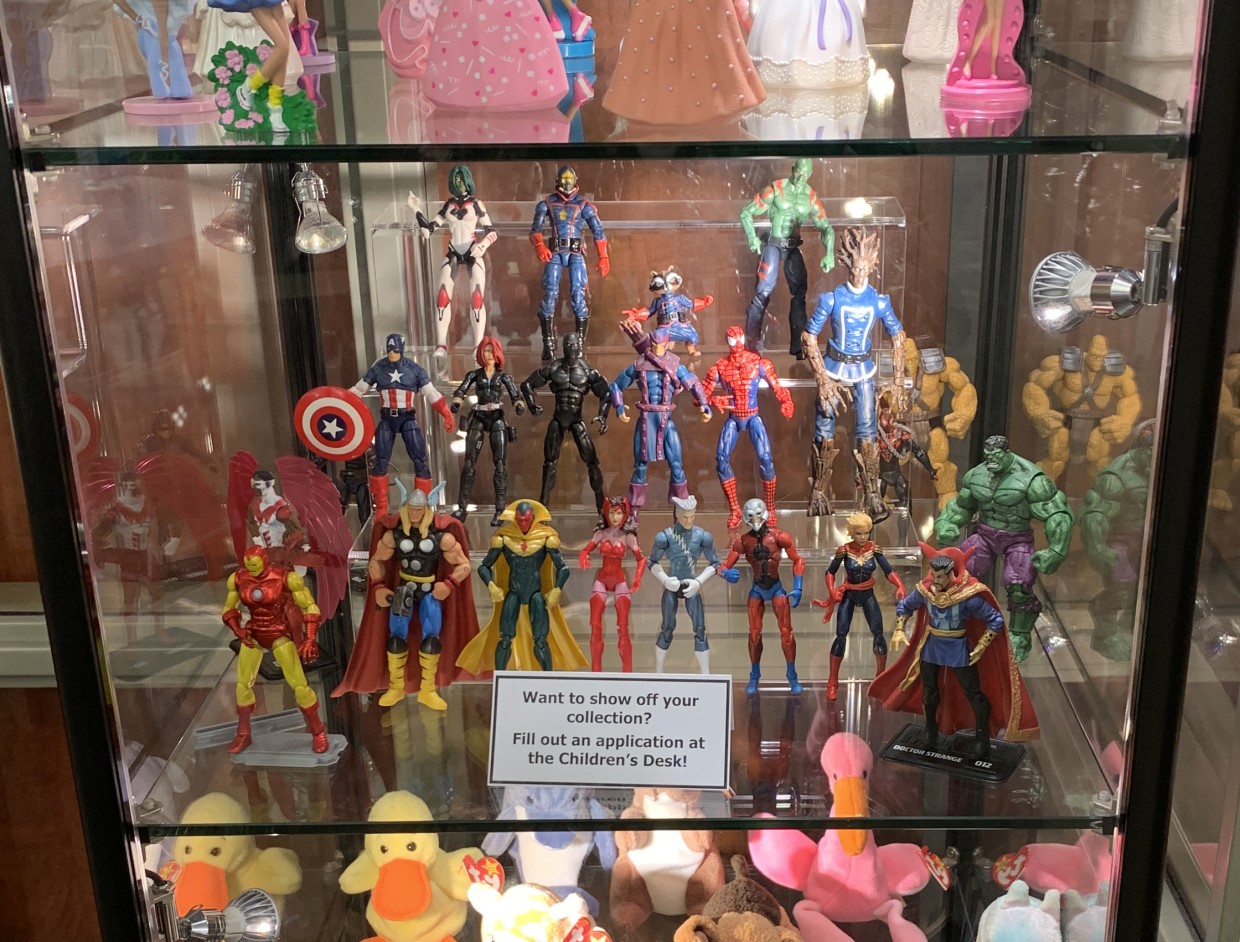 Action figures stand on a shelf of glass display case.