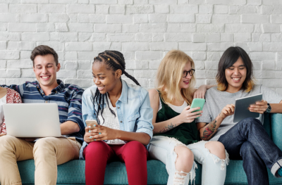 Four adults smiling and reading from electronic devices