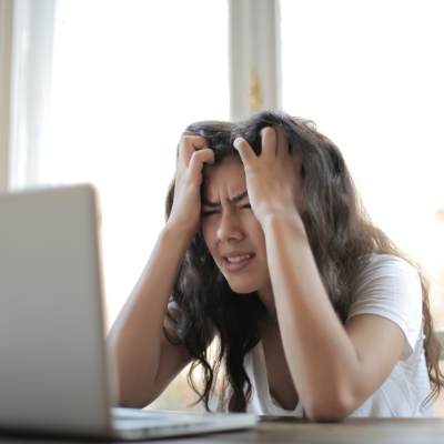 Woman sitting in front of a computer with hands in hair, clearly frustrated