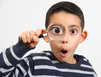 A child holding up a magnifying glass to his eye, looking surprised!