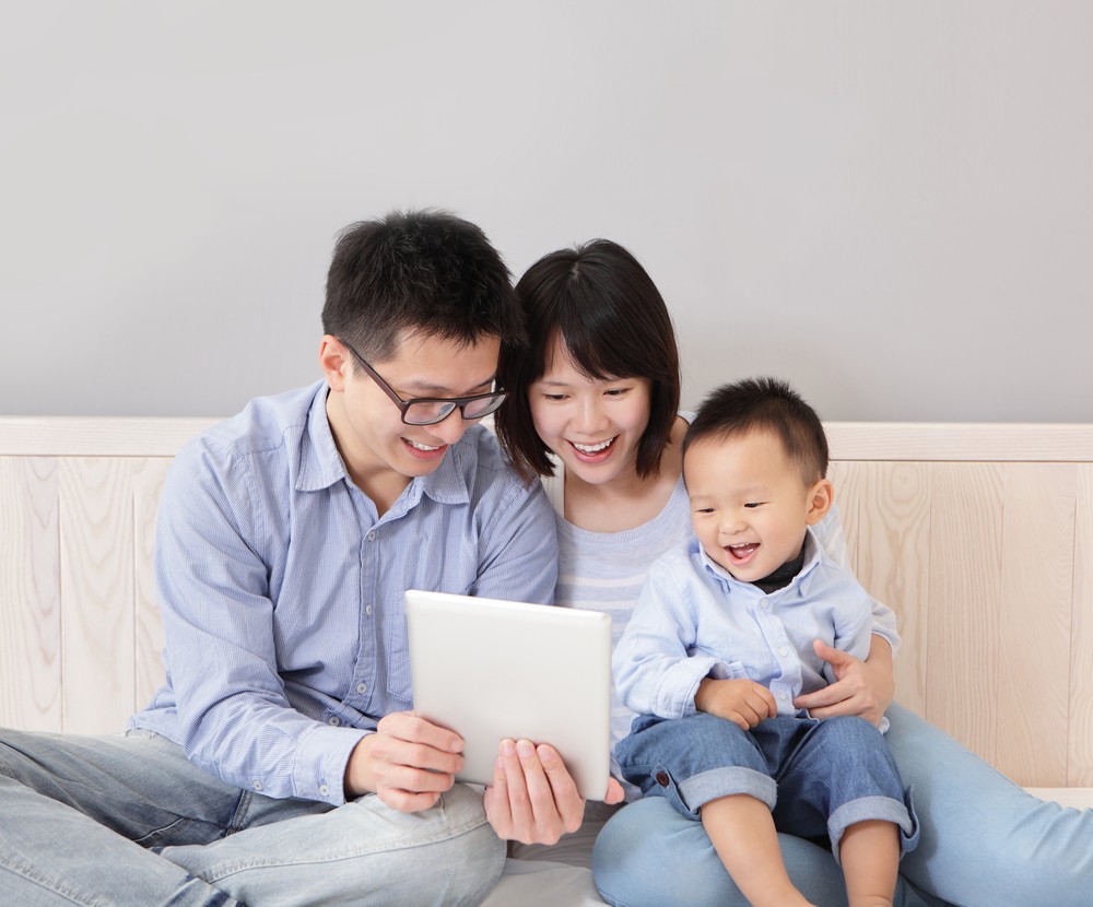 A family of three look at a tablet together, smiling and laughing