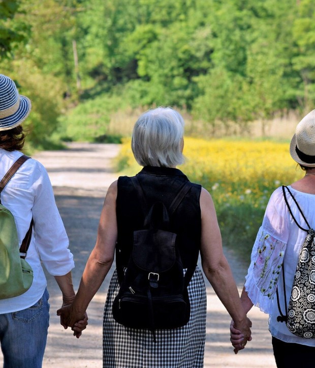 A photo taken from the back of three women walking with backpacks and holding hands
