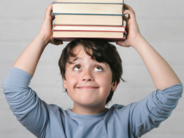 A child holds a stack of books up on their head and looks up at them