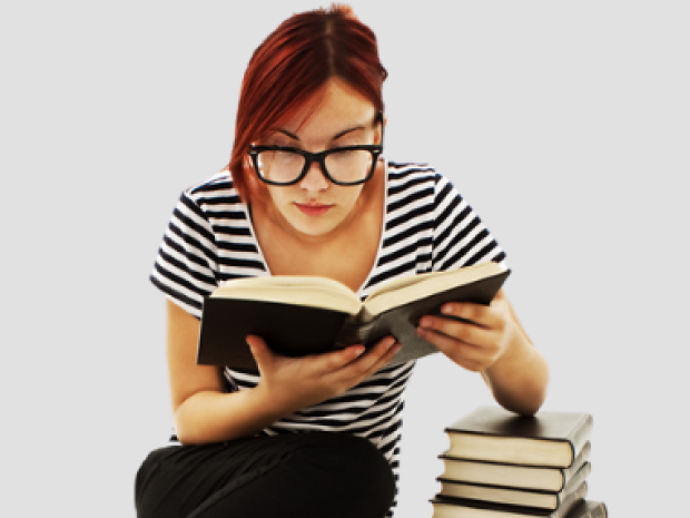 Girl reading a book with her elbow on a stack of books against a grey background