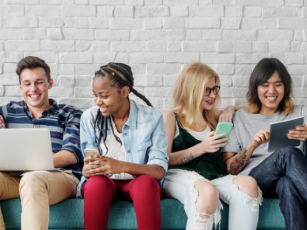 Four adults smiling and reading from electronic devices