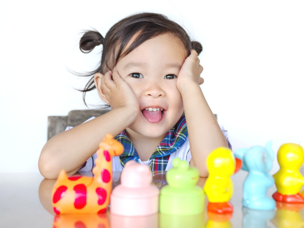 A child sits in front of a row of colorful toys, their hands on their cheeks