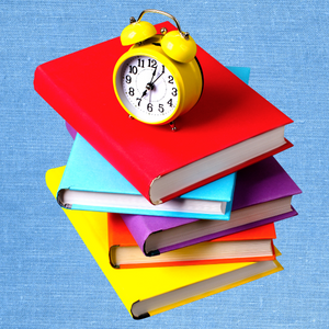 stack of mulit-colored books with a yellow alarm clock on top