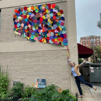 woman pretending to hold the string for a mural of several knit balloons